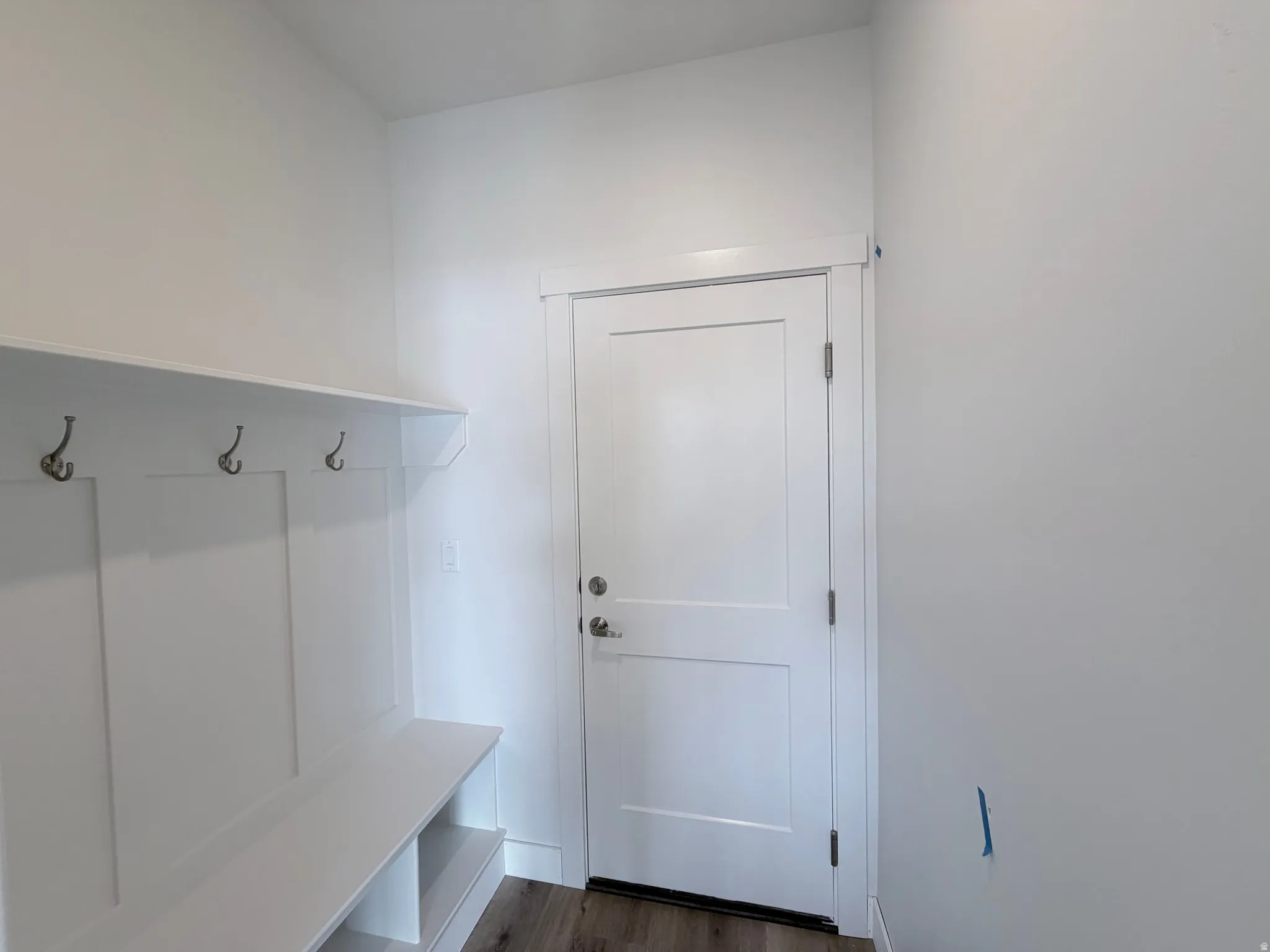 Built-in storage bench with shelving and coat hooks, white paneled door, and wood-finish flooring