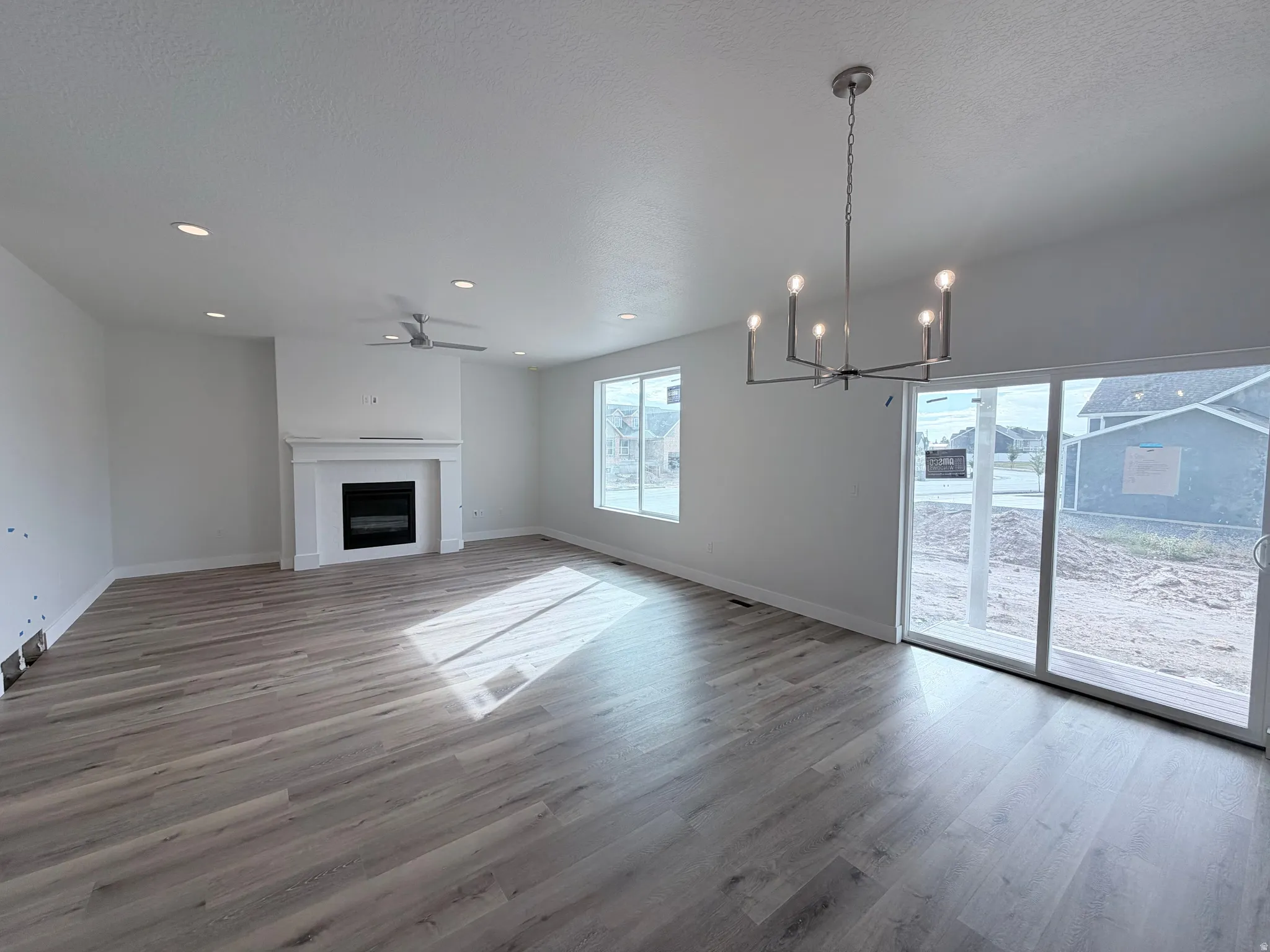 Open-concept living area featuring wood-finish flooring, a fireplace with a white mantel, recessed lighting, and a ceiling fan