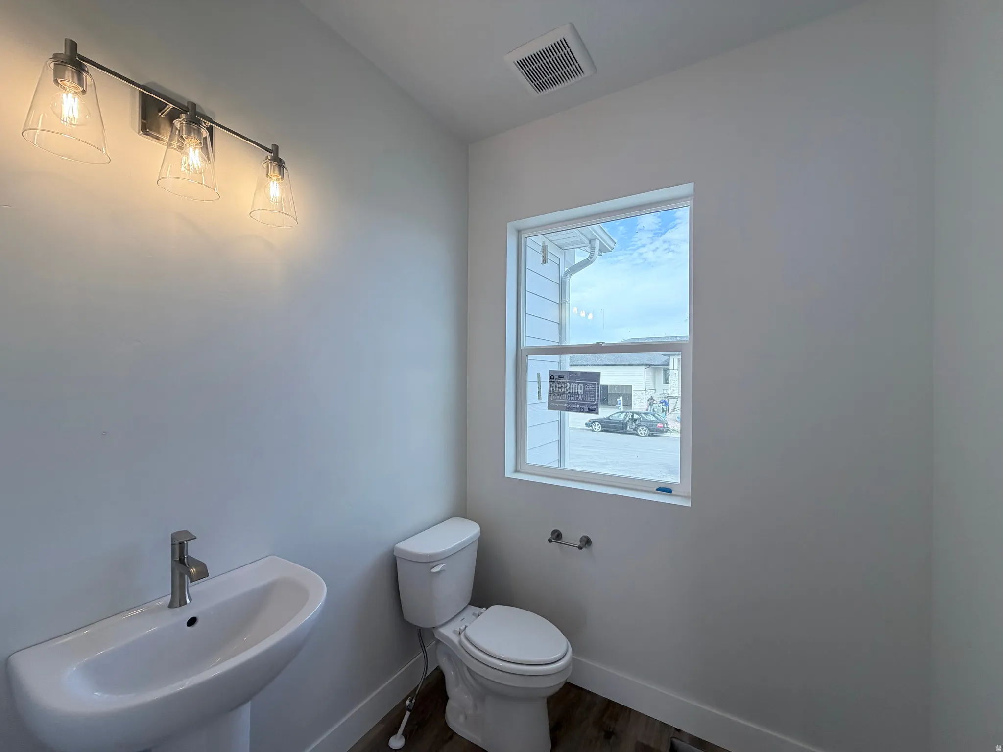 Pedestal sink with a chrome faucet, wall-mounted vanity lighting, and wood-finish flooring