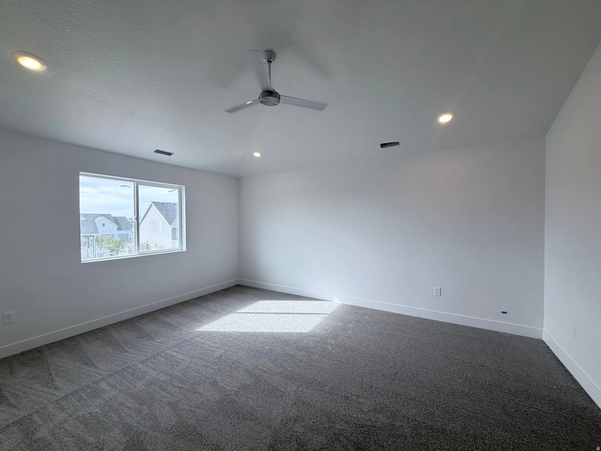 Recessed ceiling lighting, modern ceiling fan, white walls, gray carpet, and a large window