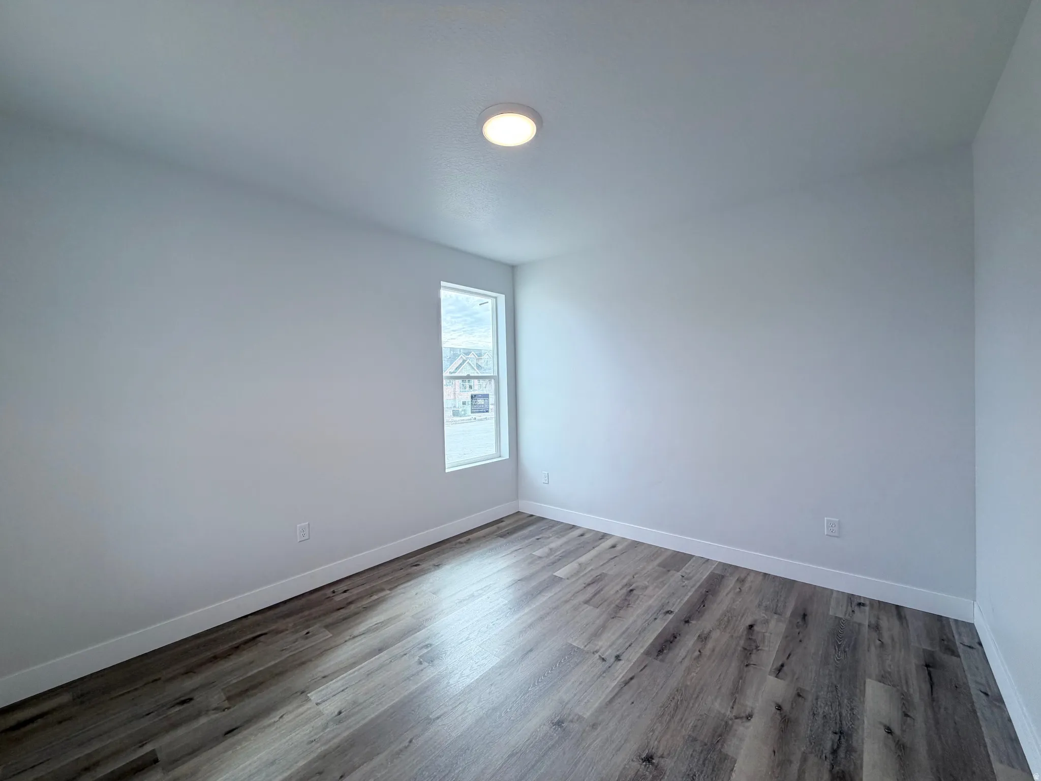 Recessed ceiling light, single window, light gray walls, wood-finish flooring, and white trim