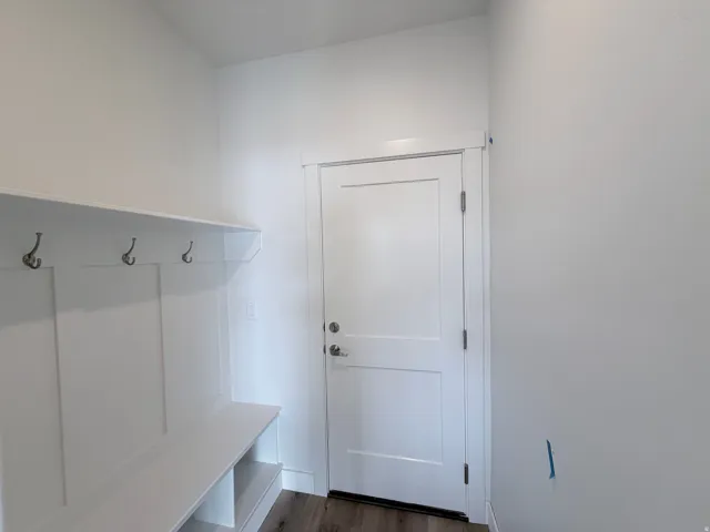 Built-in storage bench with shelving and coat hooks, white paneled door, and wood-finish flooring