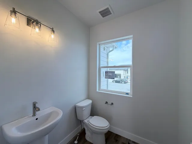 Pedestal sink with a chrome faucet, wall-mounted vanity lighting, and wood-finish flooring