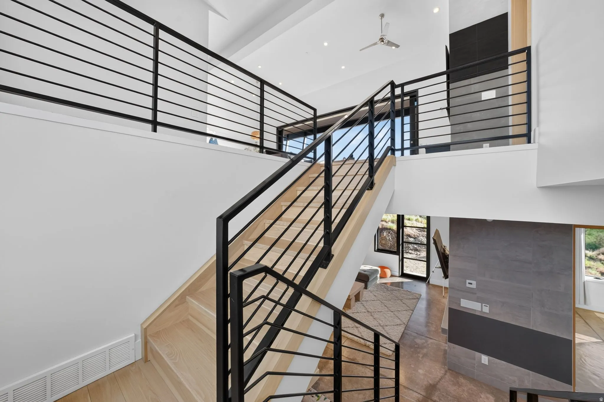 Modern open-tread staircase with black metal railings and light wood steps, high vaulted ceilings, recessed lighting, and a ceiling fan