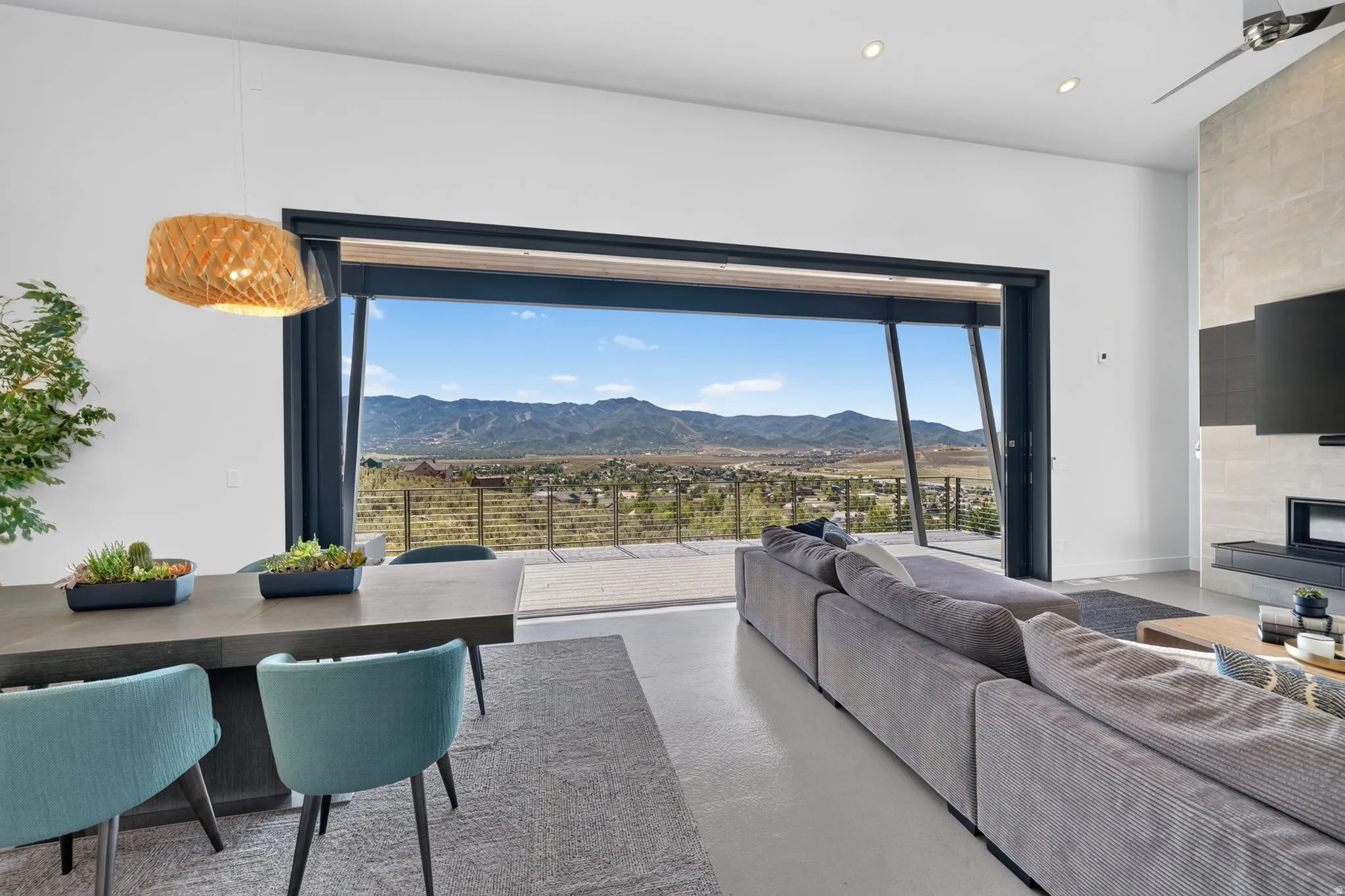 Expansive sliding glass doors, concrete flooring, a modern fireplace with a stone surround, and an integrated ceiling fan