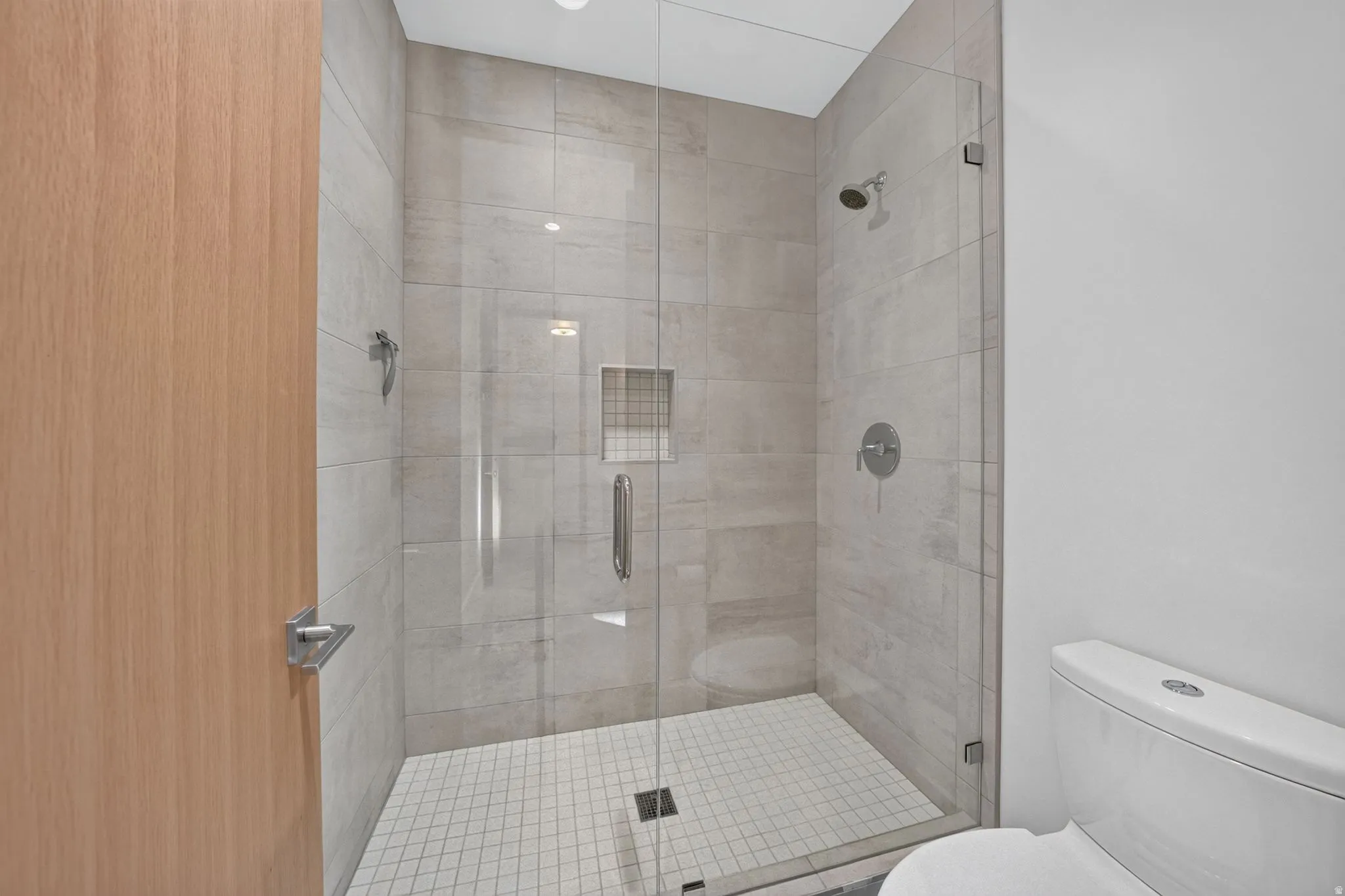Glass-enclosed shower with large format tile walls, mosaic tile floor, and a recessed shower niche