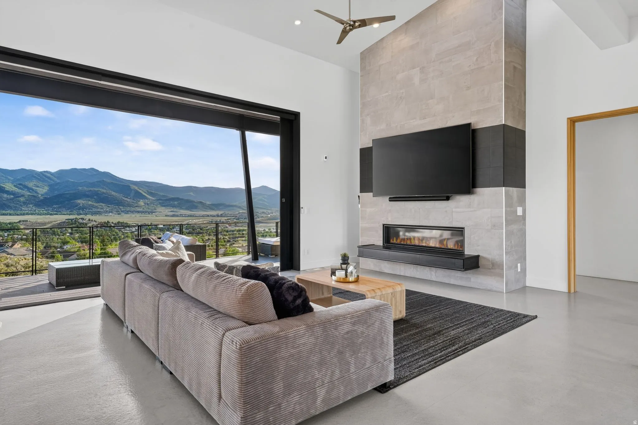 Expansive sliding glass doors, contemporary fireplace with a sleek hearth, high ceilings, ceiling fan, and concrete flooring