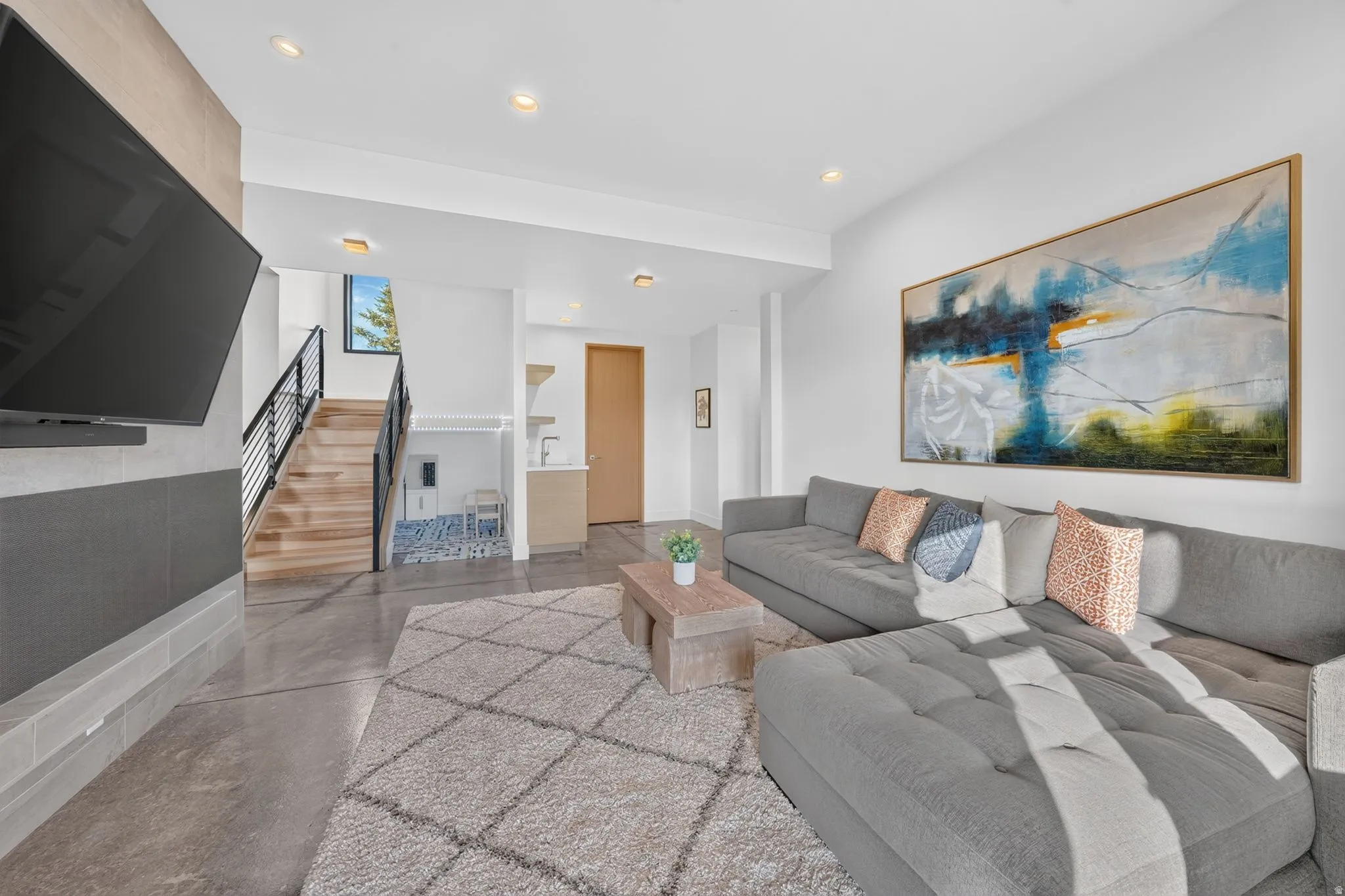 Polished concrete flooring, recessed lighting, wood-finish staircase with black metal railing, and a built-in media wall