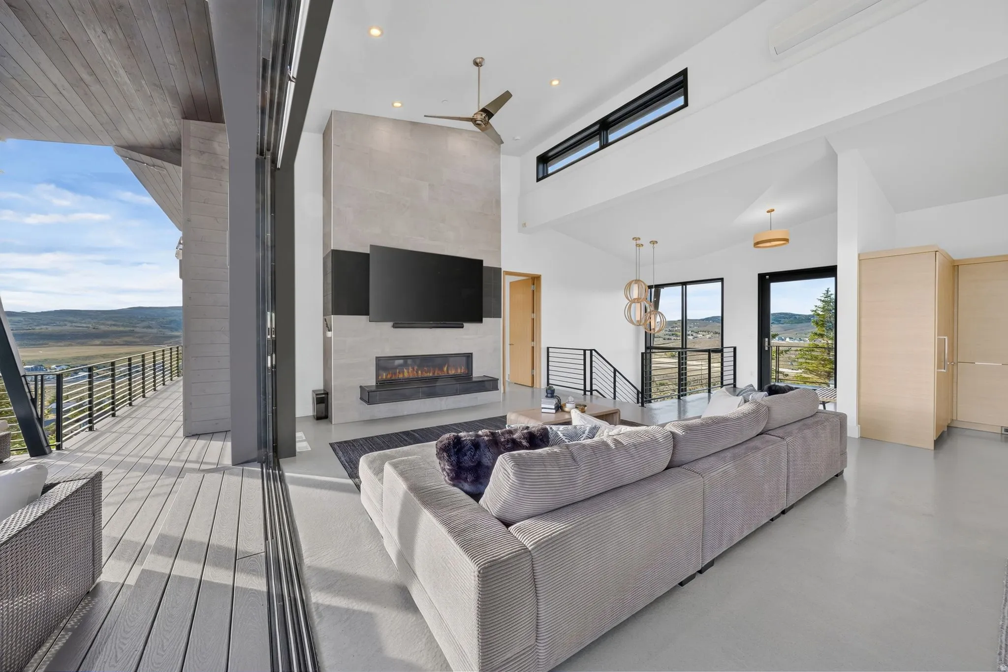Open-concept living area with vaulted ceilings, a built-in linear fireplace, and a spacious outdoor deck