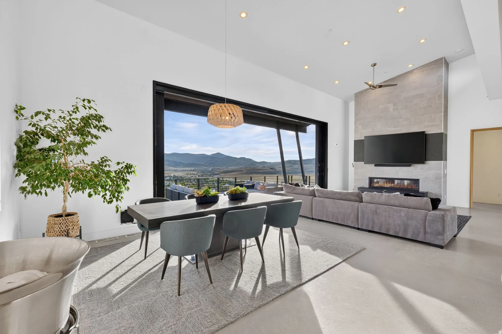 Expansive open-concept living area featuring a floor-to-ceiling fireplace with integrated linear firebox, soaring vaulted ceilings, and a large multi-panel sliding glass door