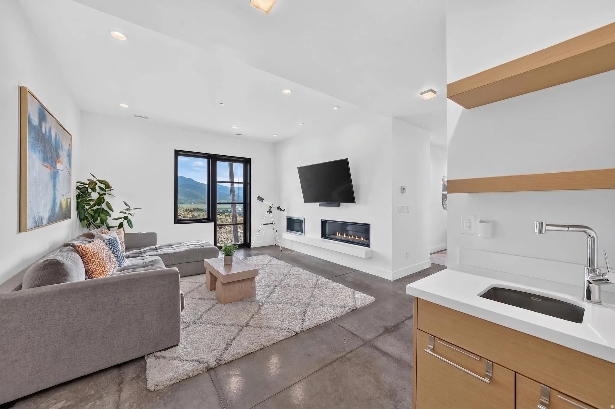 Built-in linear fireplace, recessed lighting, floor-to-ceiling black-framed window, built-in wet bar with stainless steel faucet, and open wood shelving