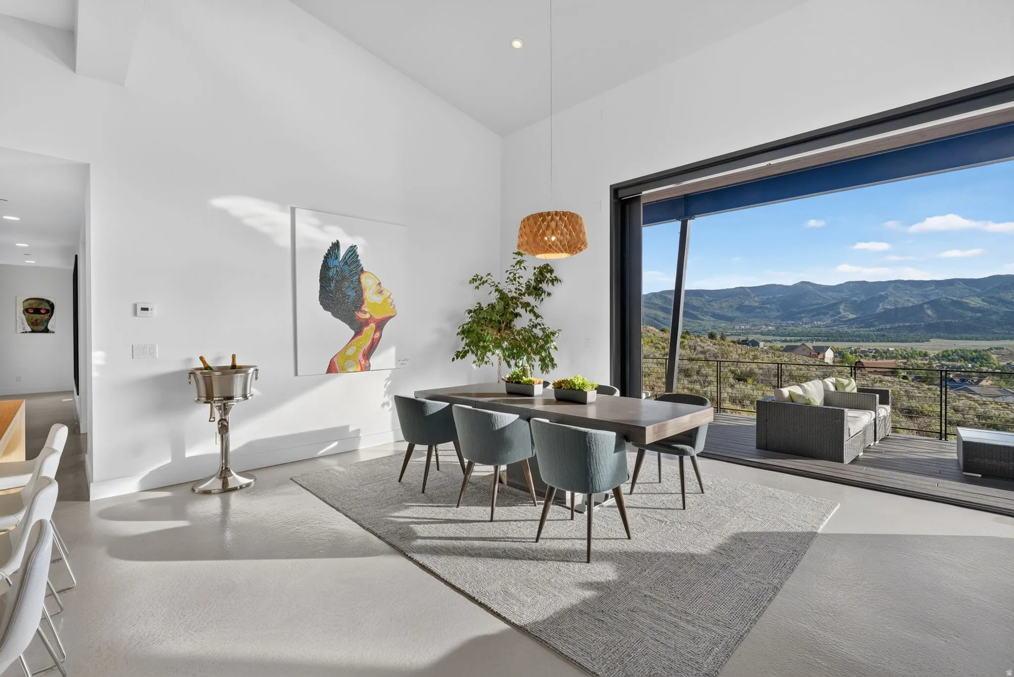 Expansive sliding glass doors, pitched ceiling, recessed lighting, and durable flooring, opening to an exterior deck with mountain scenery