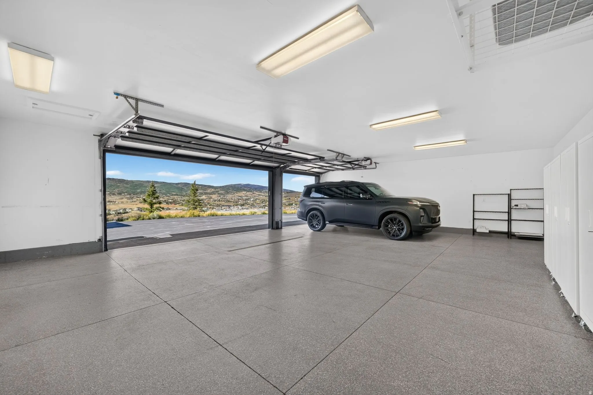 Expansive garage with epoxy flooring, multiple fluorescent lighting fixtures, and built-in storage cabinetry