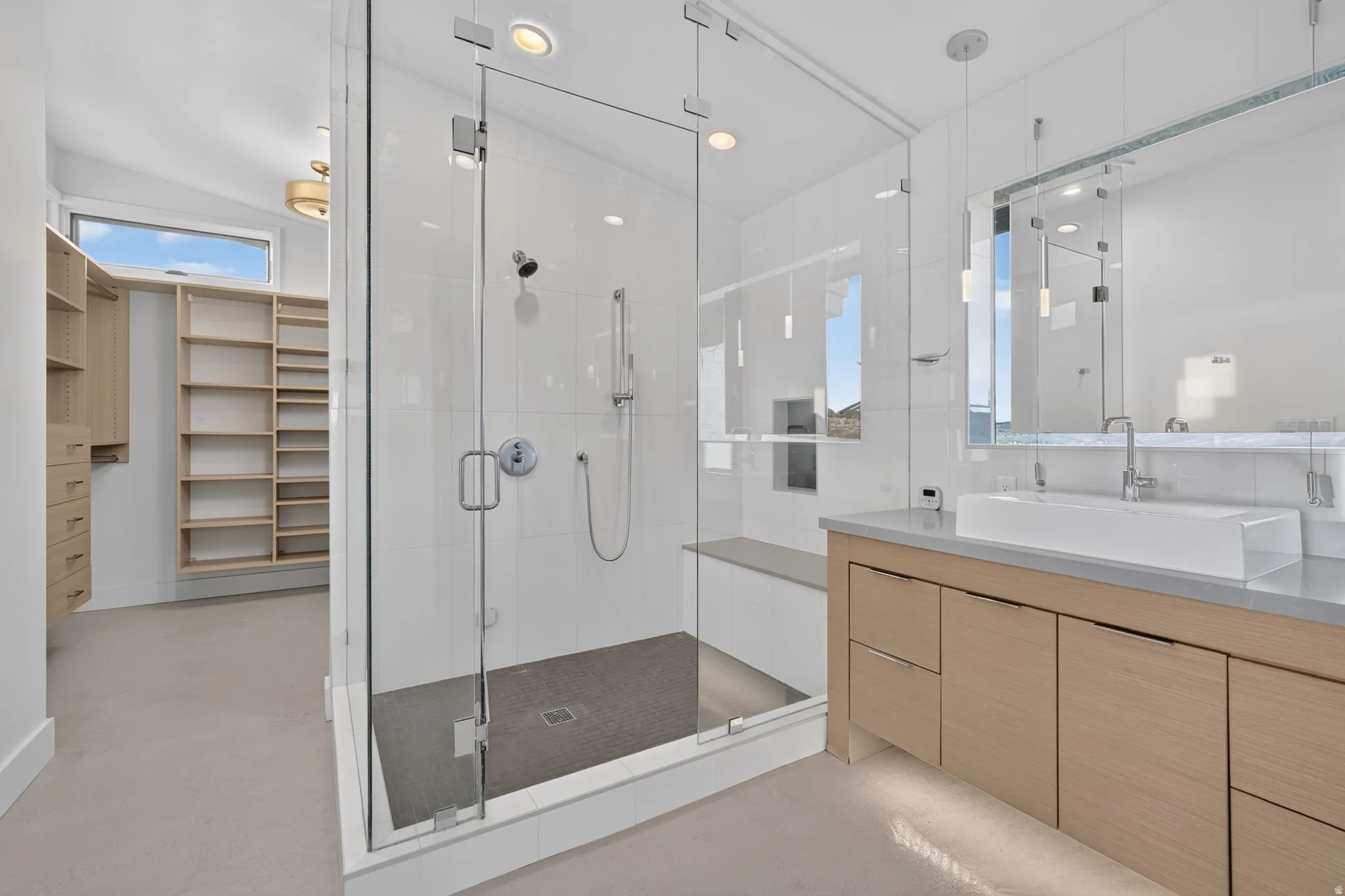 Glass-enclosed shower with a built-in bench, a wood-finish double vanity with a vessel sink, and an expansive walk-in closet with built-in shelving