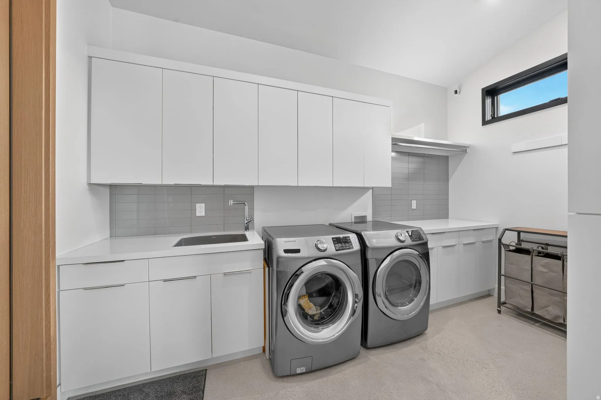 Integrated laundry room with white cabinetry, a built-in sink, and light-toned countertops