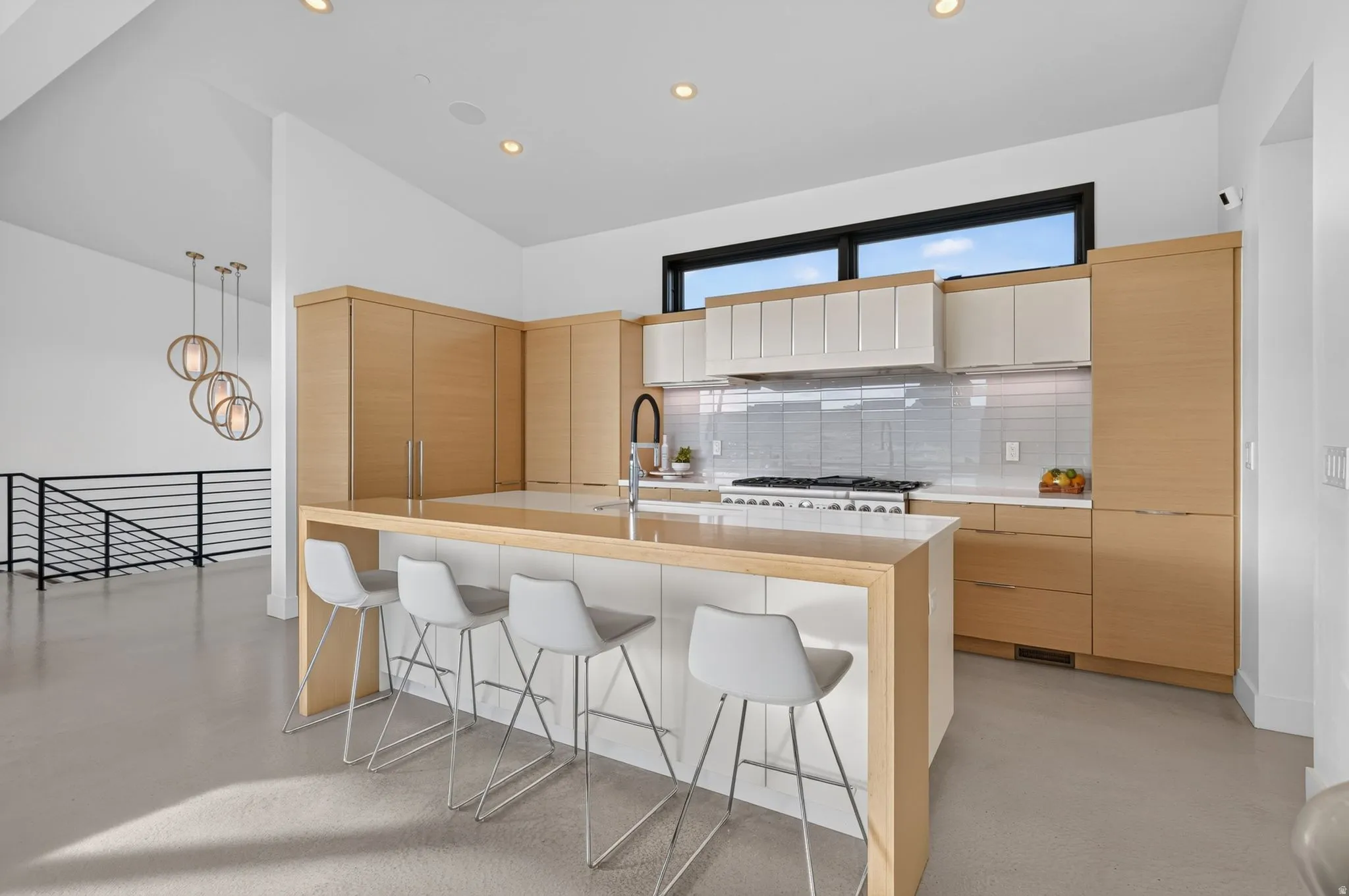 Kitchen featuring a large island with integrated seating, light wood-finish cabinetry, white countertops, a tile backsplash, and a range with a hood