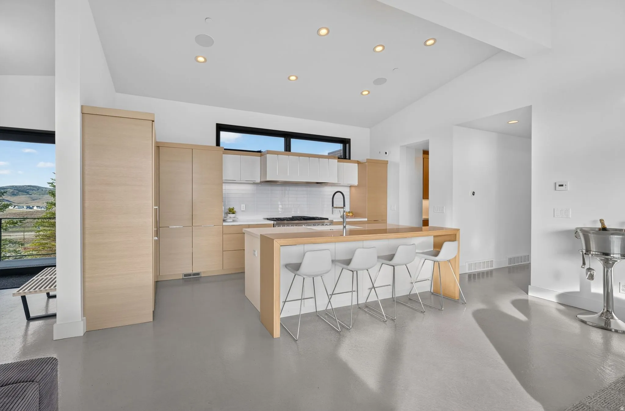 Modern kitchen featuring light wood-finish cabinetry, white upper cabinets, an integrated refrigerator, a center island with seating, and a white subway tile backsplash