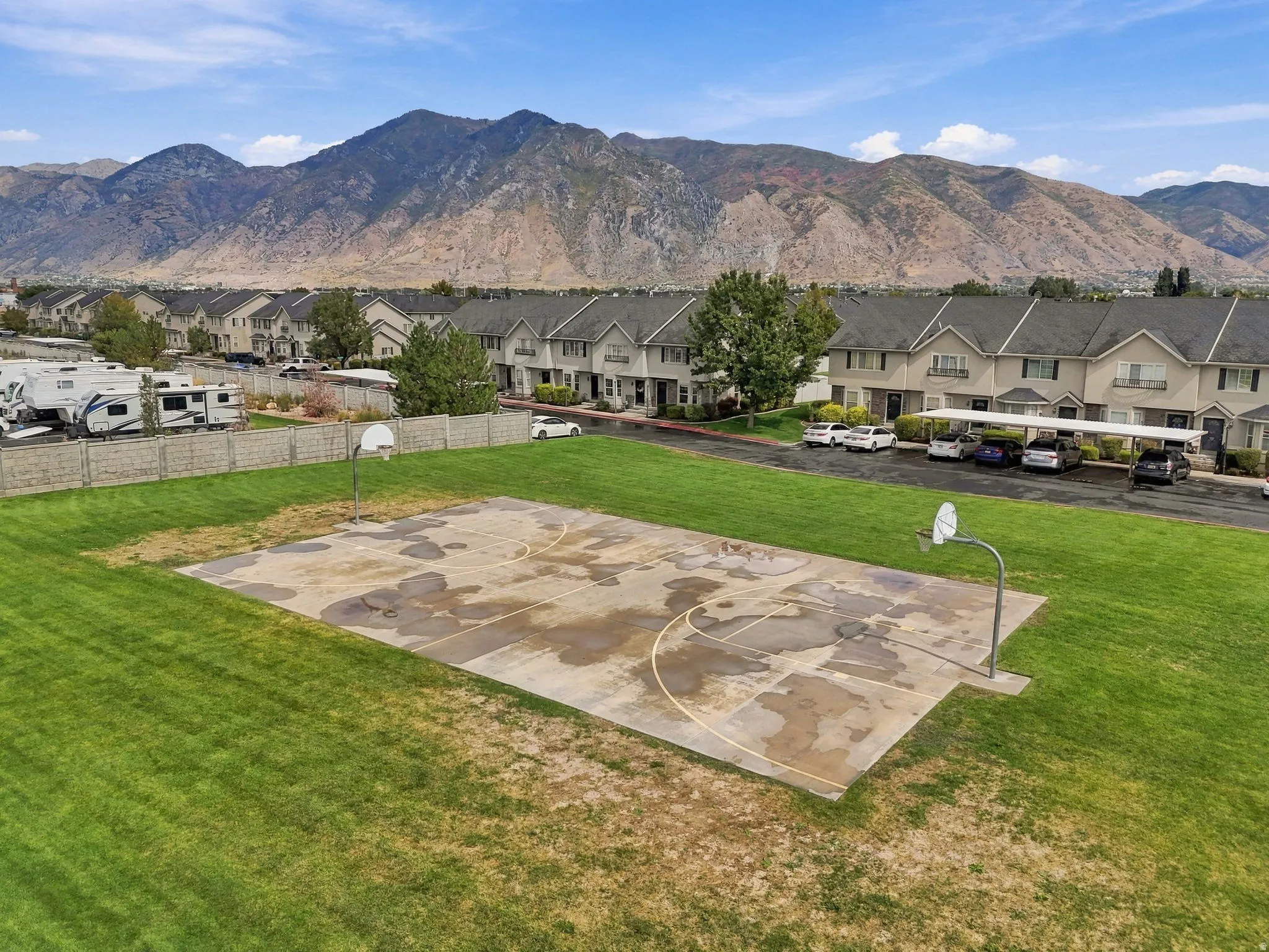 Outdoor basketball court with two hoops, surrounded by a grassy area and framed by distant mountains