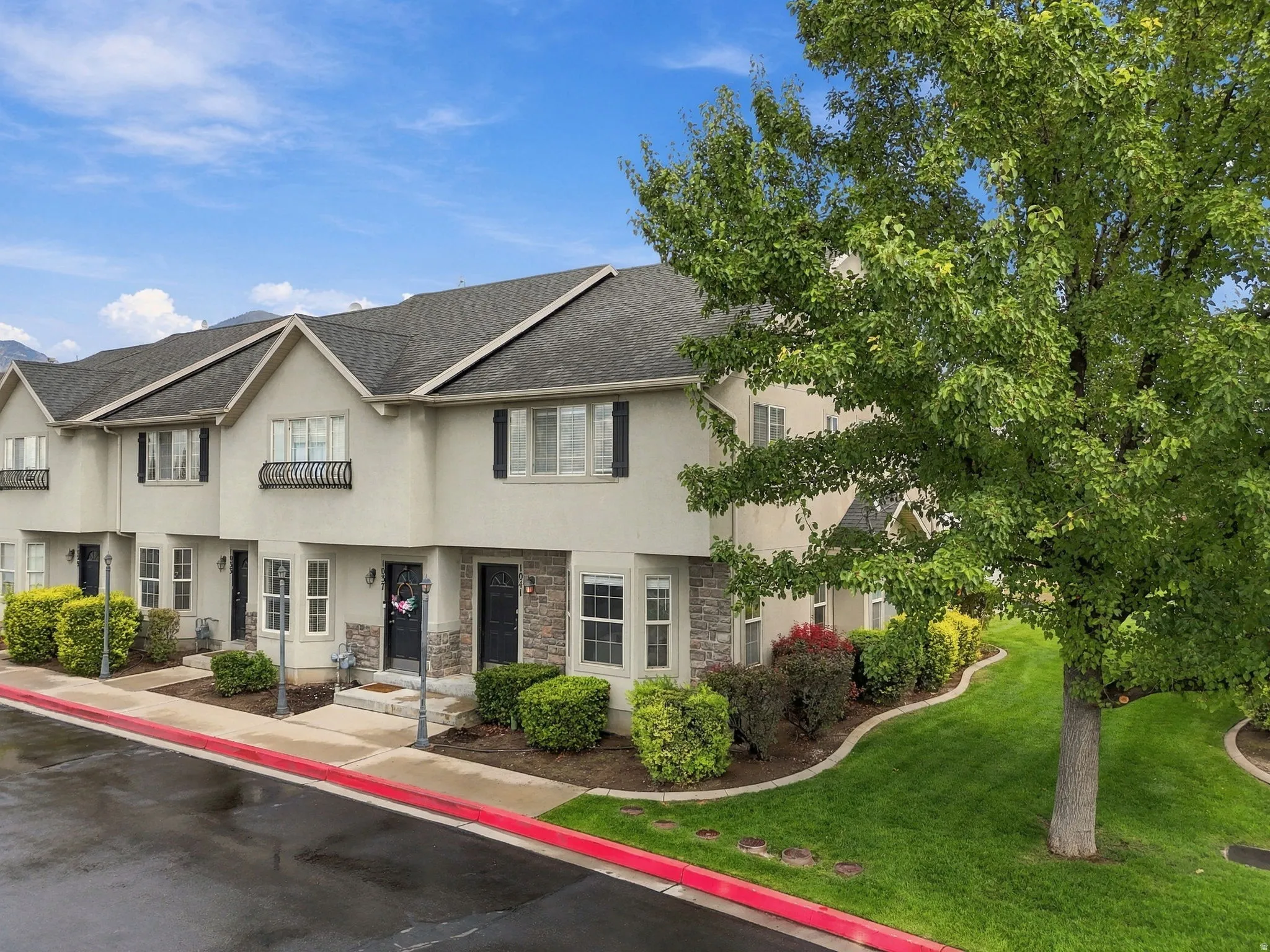 Multi-level townhome exterior with stone accents, black shutters, and mature landscaping