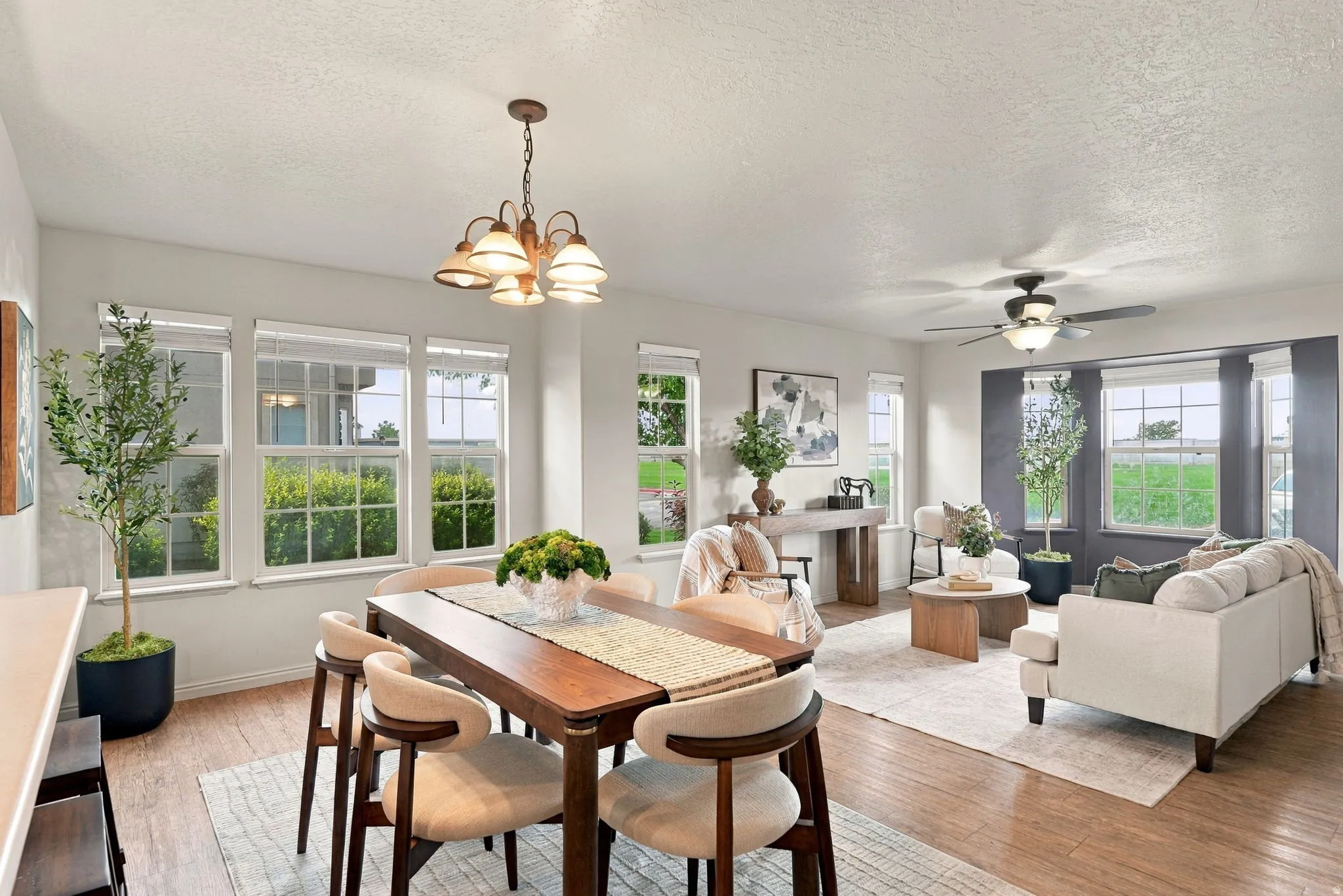 Open-concept living area with wood-finish flooring, multiple windows, and a dining area featuring a suspended light fixture