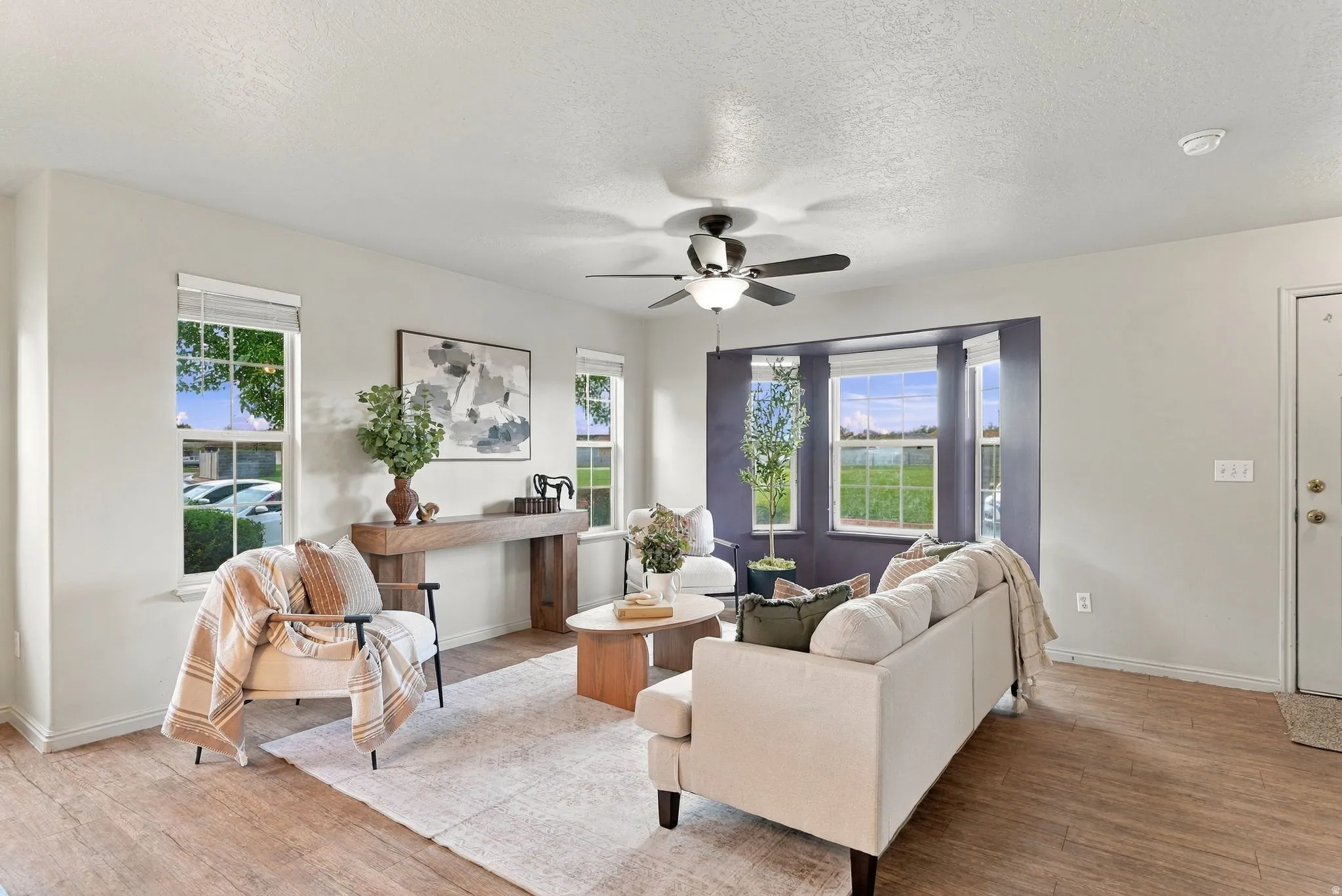Wood-finish flooring, multiple windows, ceiling fan with integrated lighting, and a bay window feature in this living area