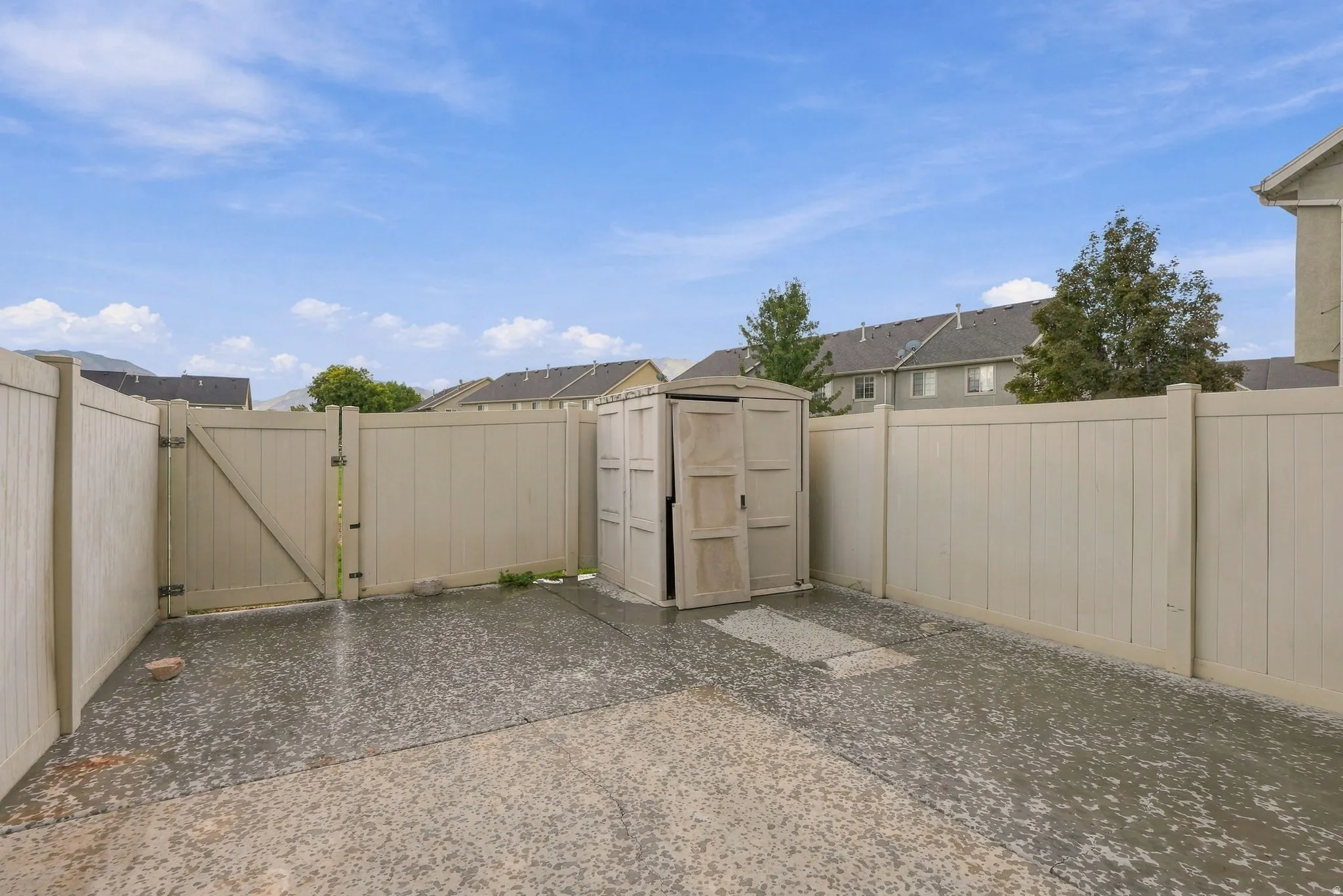 Fenced outdoor area featuring a double gate, paved surface, and a built-in storage shed