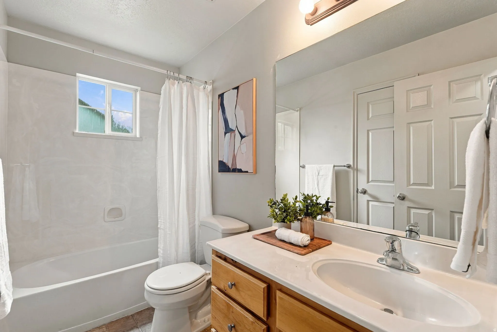 Bathroom featuring a windowed shower-tub combination with white surround, a vanity with wood-finish cabinetry, a single basin sink, and an expansive mirror