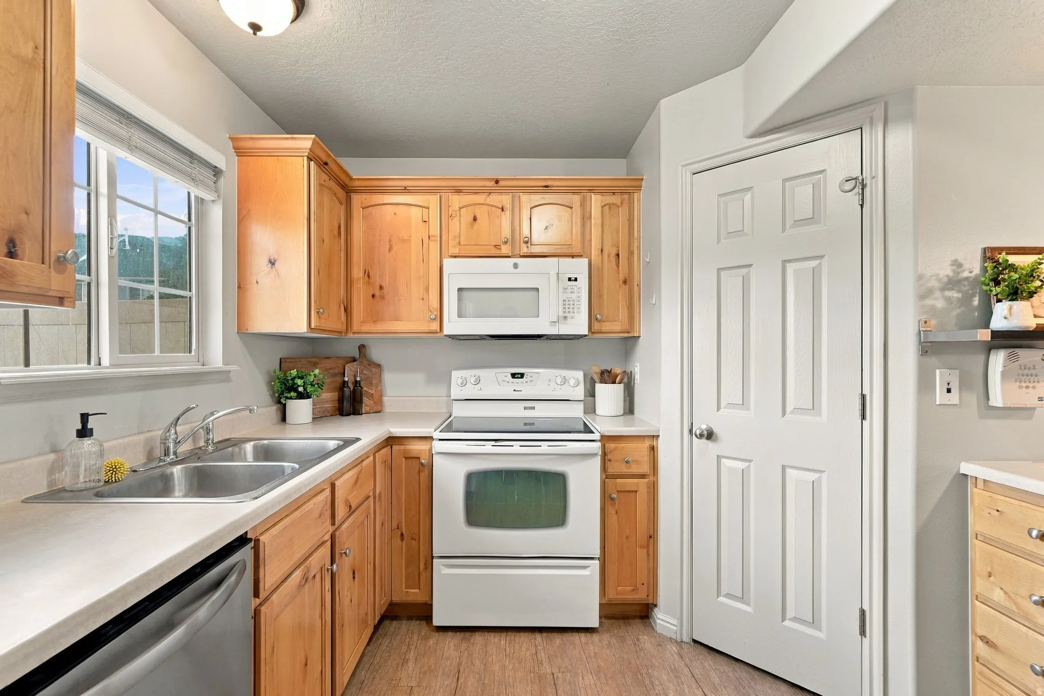 Kitchen featuring wood-finish cabinetry, white appliances, dual stainless steel sink, and wood-look flooring
