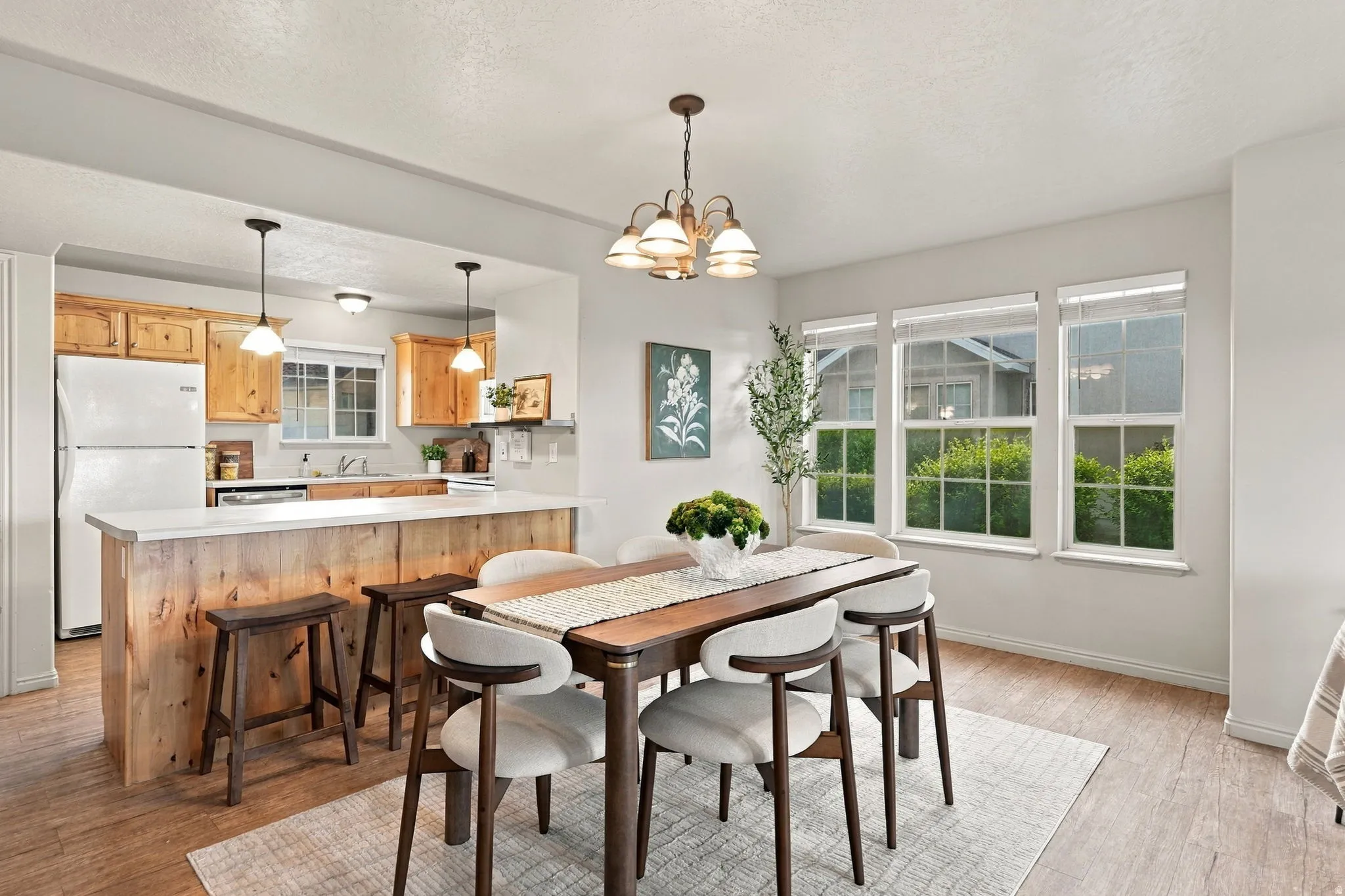 Open-concept living space featuring wood-finish flooring, a kitchen island with seating, a dining area with a chandelier, and multiple windows