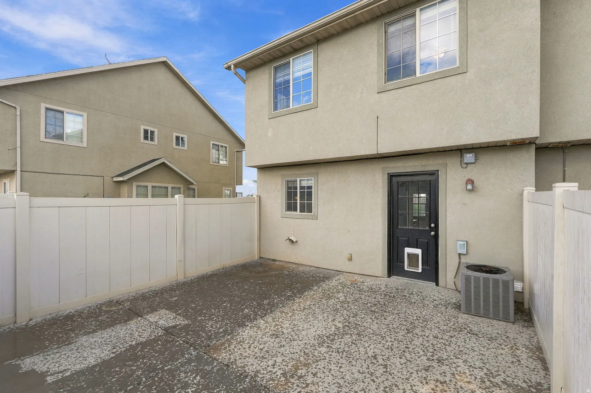 Enclosed patio area with a privacy fence, concrete surface, and stucco exterior