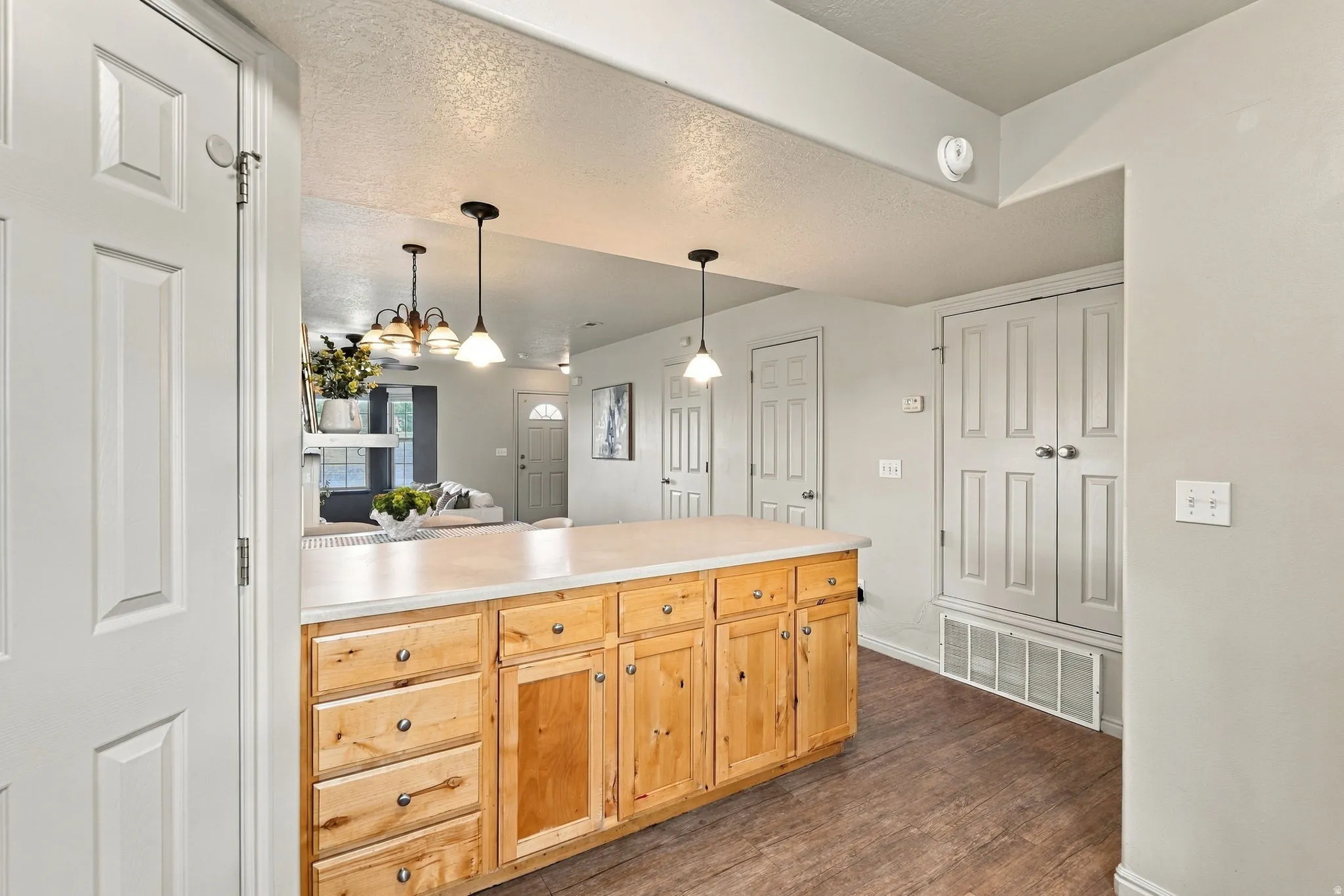 Kitchen island with light wood cabinetry, a light-toned countertop, and pendant lighting