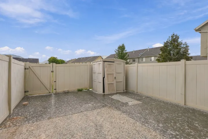 Fenced outdoor area featuring a double gate, paved surface, and a built-in storage shed
