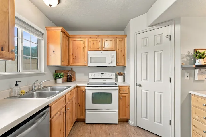 Kitchen featuring wood-finish cabinetry, white appliances, dual stainless steel sink, and wood-look flooring