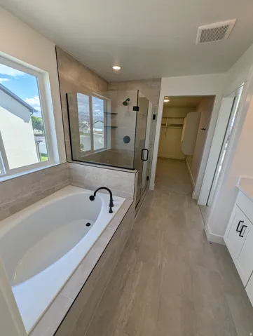 Soaking tub with matte black faucet, walk-in shower with glass enclosure, tiled walls, recessed lighting, and tile flooring