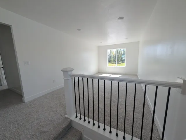 Carpeted upper-level space featuring a window, recessed lighting, and a white railing with black balusters