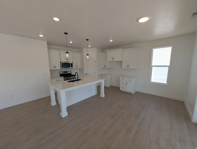 Kitchen with white cabinetry, stainless steel appliances, a center island with sink, pendant lighting, and wood-finish flooring