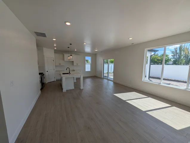 Open-concept living area featuring wood-finish flooring, recessed lighting, white cabinetry, a kitchen island with a dark faucet, and a large window
