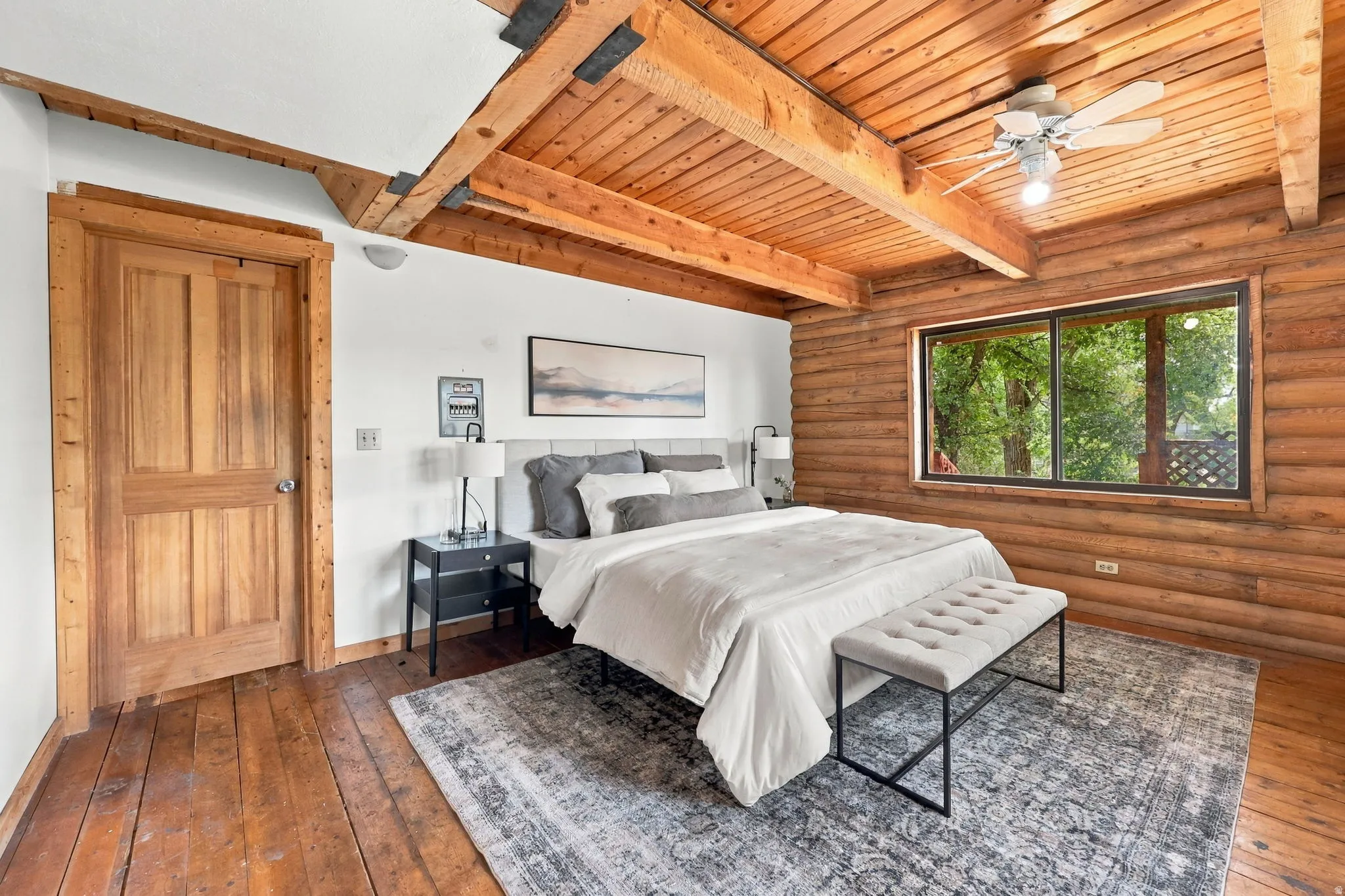 Wood-paneled ceiling with exposed beams, log wall construction, wood-finish flooring, and a ceiling fan