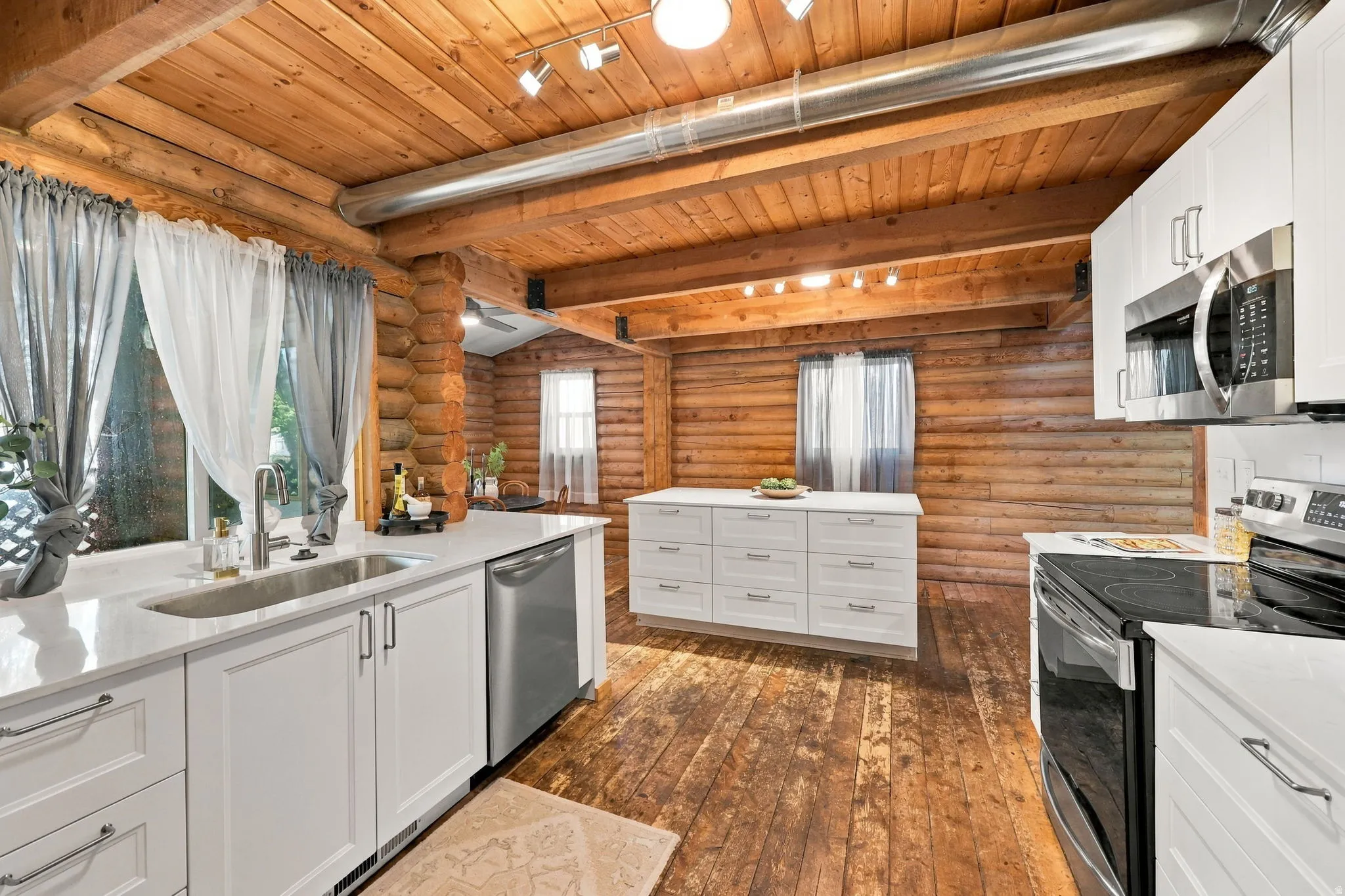 Kitchen featuring white cabinetry, stainless steel appliances, a center island with storage, and exposed log walls