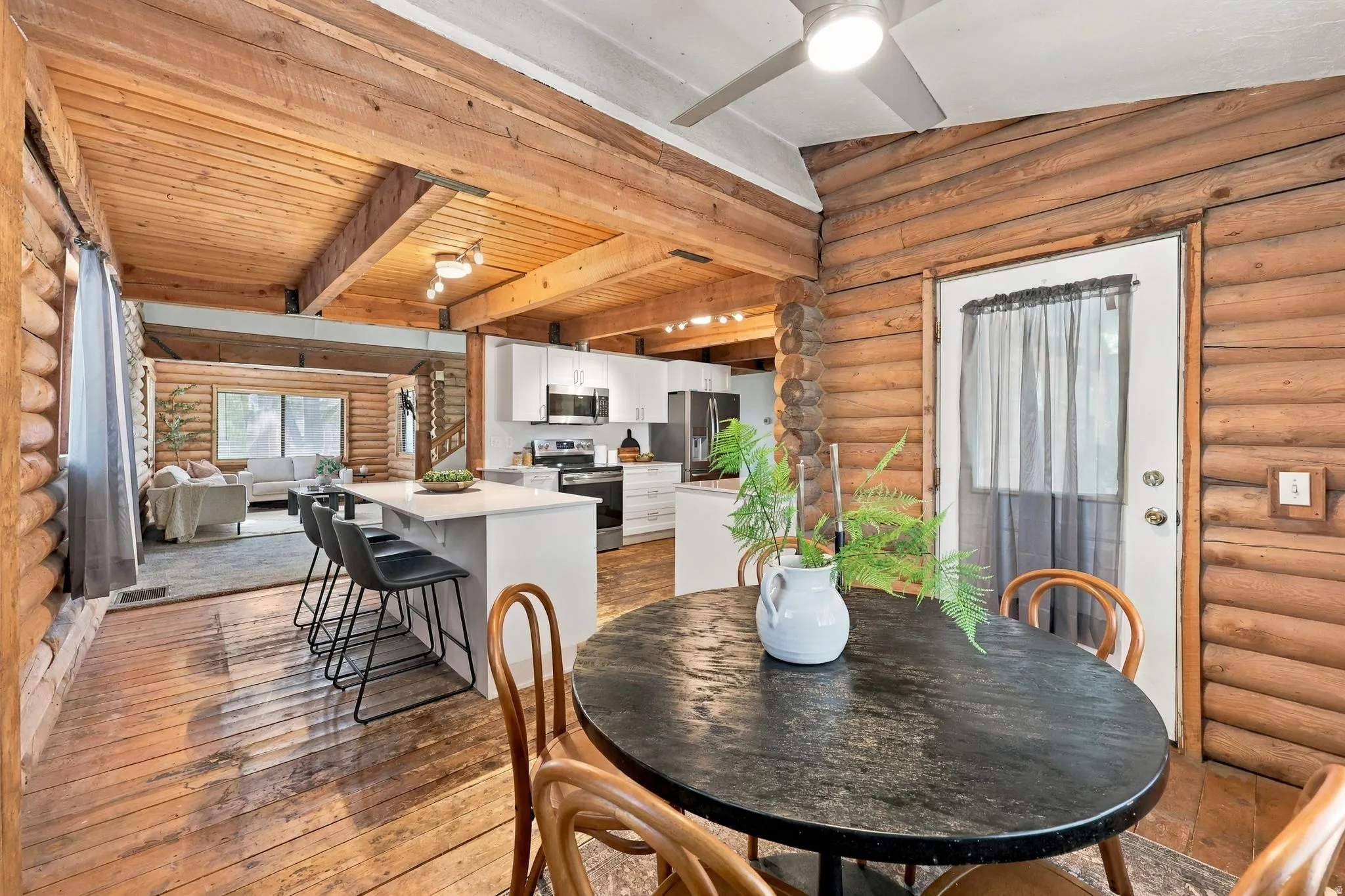 Open-concept living space featuring wood-finish flooring, exposed wood beam ceiling, and a kitchen island with seating