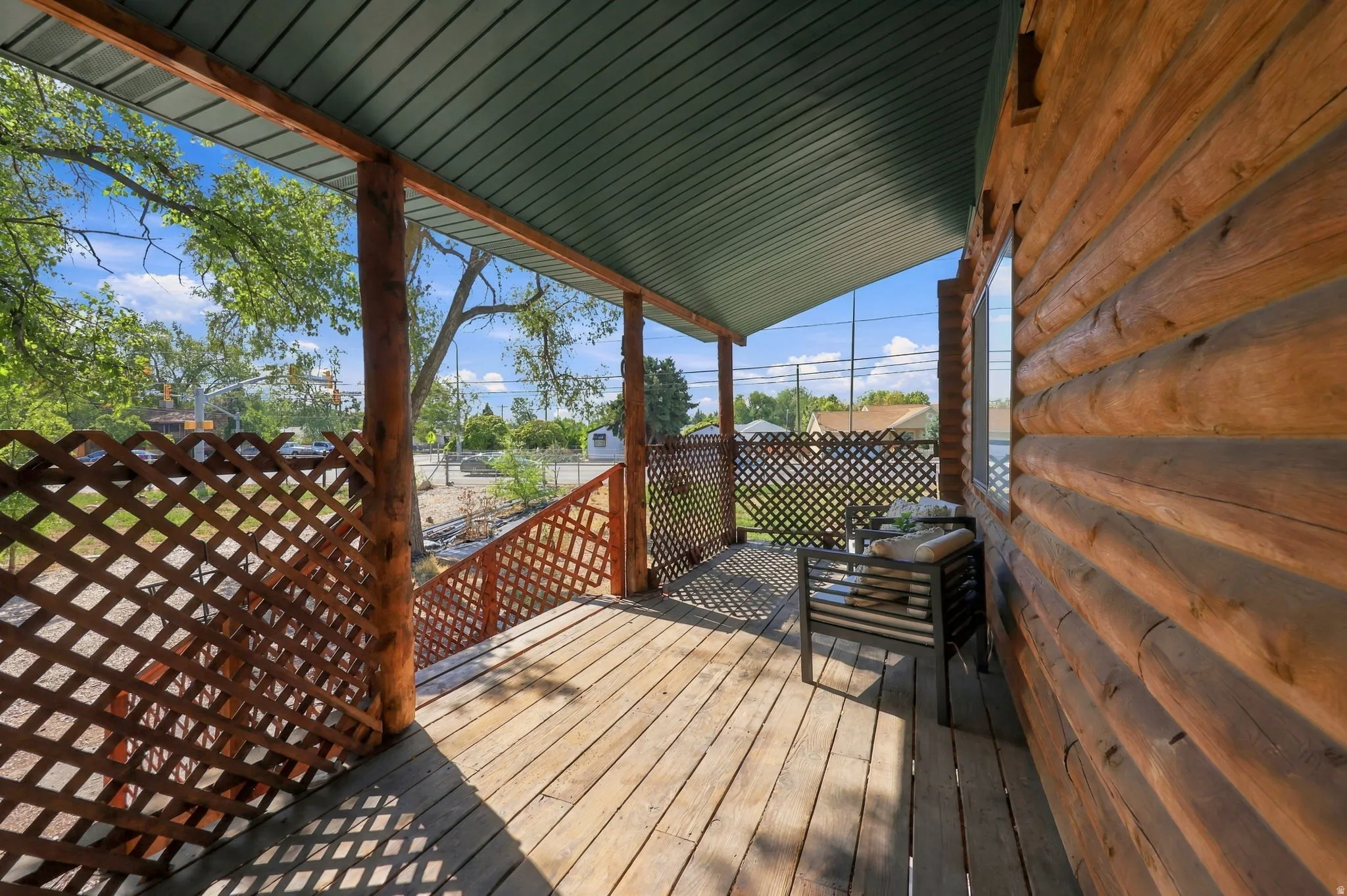 Covered log cabin porch with wood-finish decking, log-style columns, and latticework railings