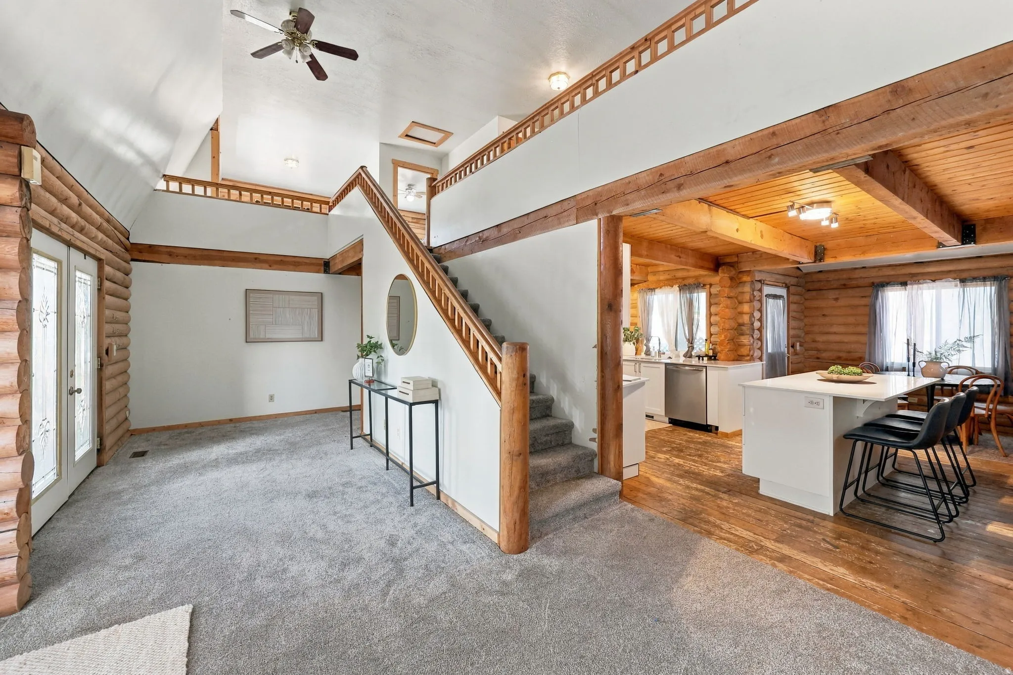 Vaulted ceiling with exposed beams, wood-finish flooring, two-story entryway, built-in staircase, and kitchen island with countertop seating