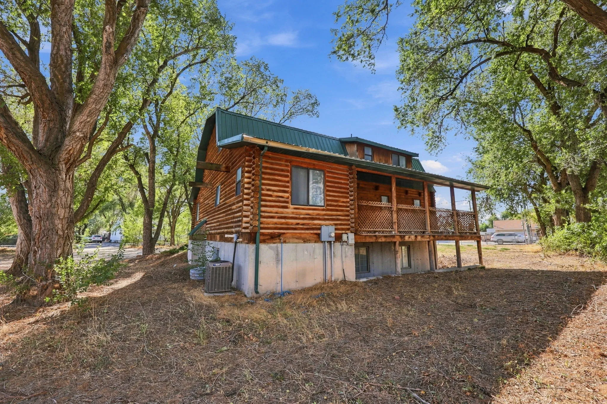 Log cabin construction with a green metal roof, covered porch, and exposed concrete foundation