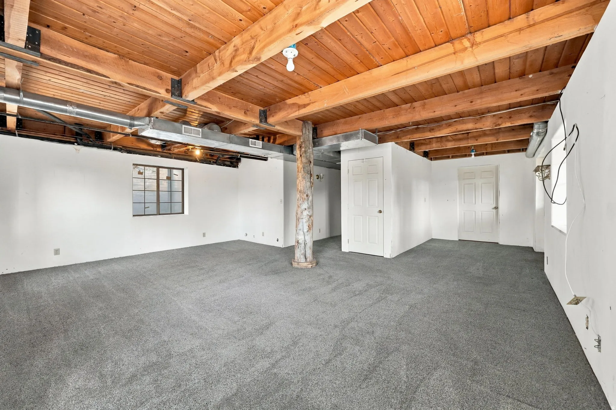 Exposed wood beam ceiling, carpet flooring, multiple white doors, exposed ductwork, and a single-pane window