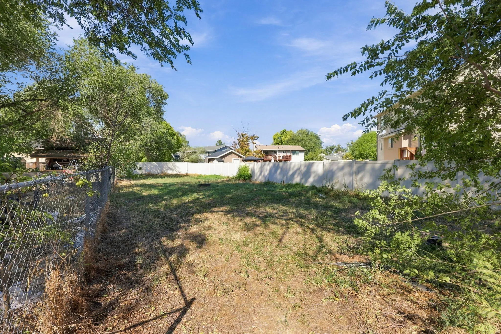 Expansive lot with a chain-link fence, concrete perimeter wall, and mature foliage