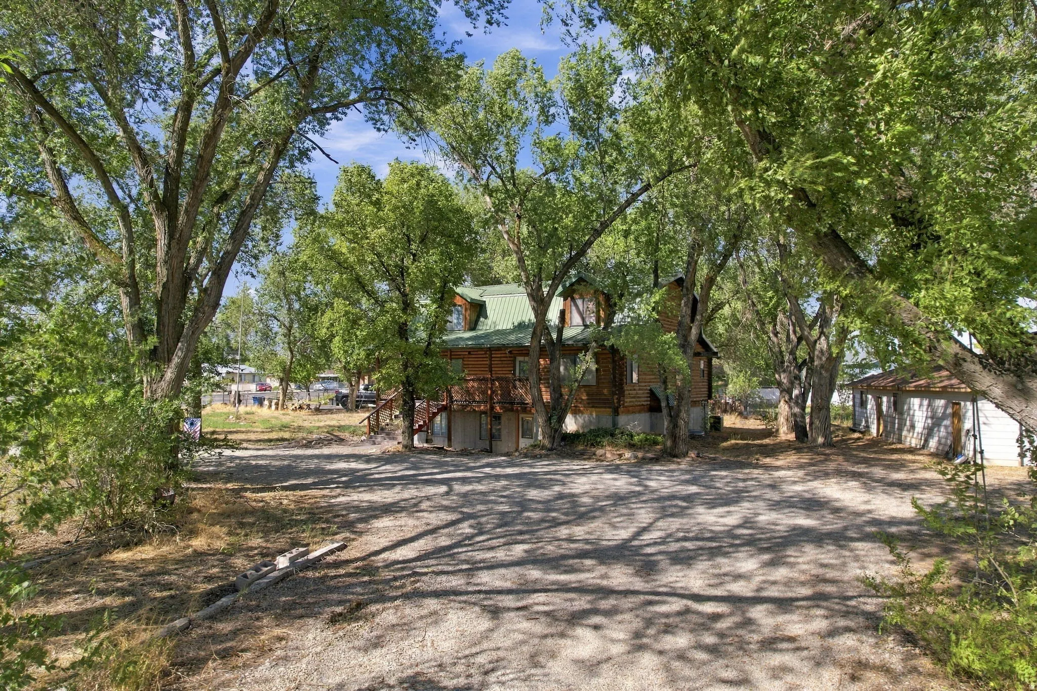 Log-sided residence featuring a green metal roof, elevated deck, and mature trees on a gravel lot