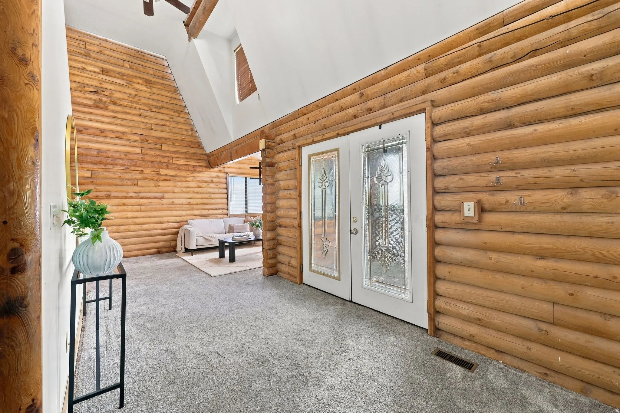 Double entry doors with decorative glass panels, full log wall construction, and a sloped ceiling with exposed wood beams