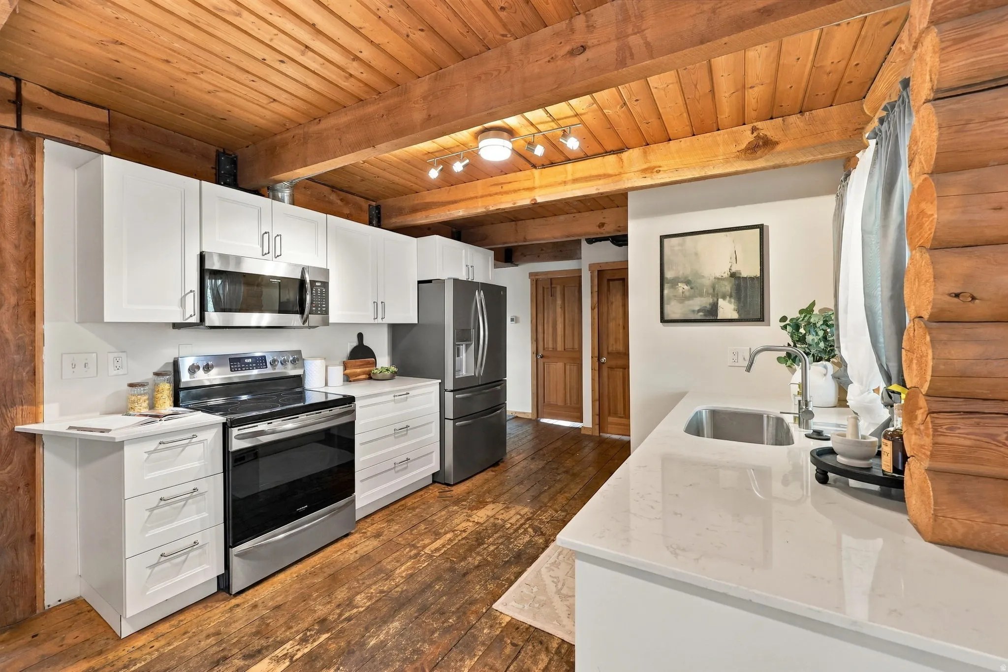 Wood-plank ceiling, exposed wood beams, wood-finish flooring, white cabinetry, and a stainless steel appliance suite