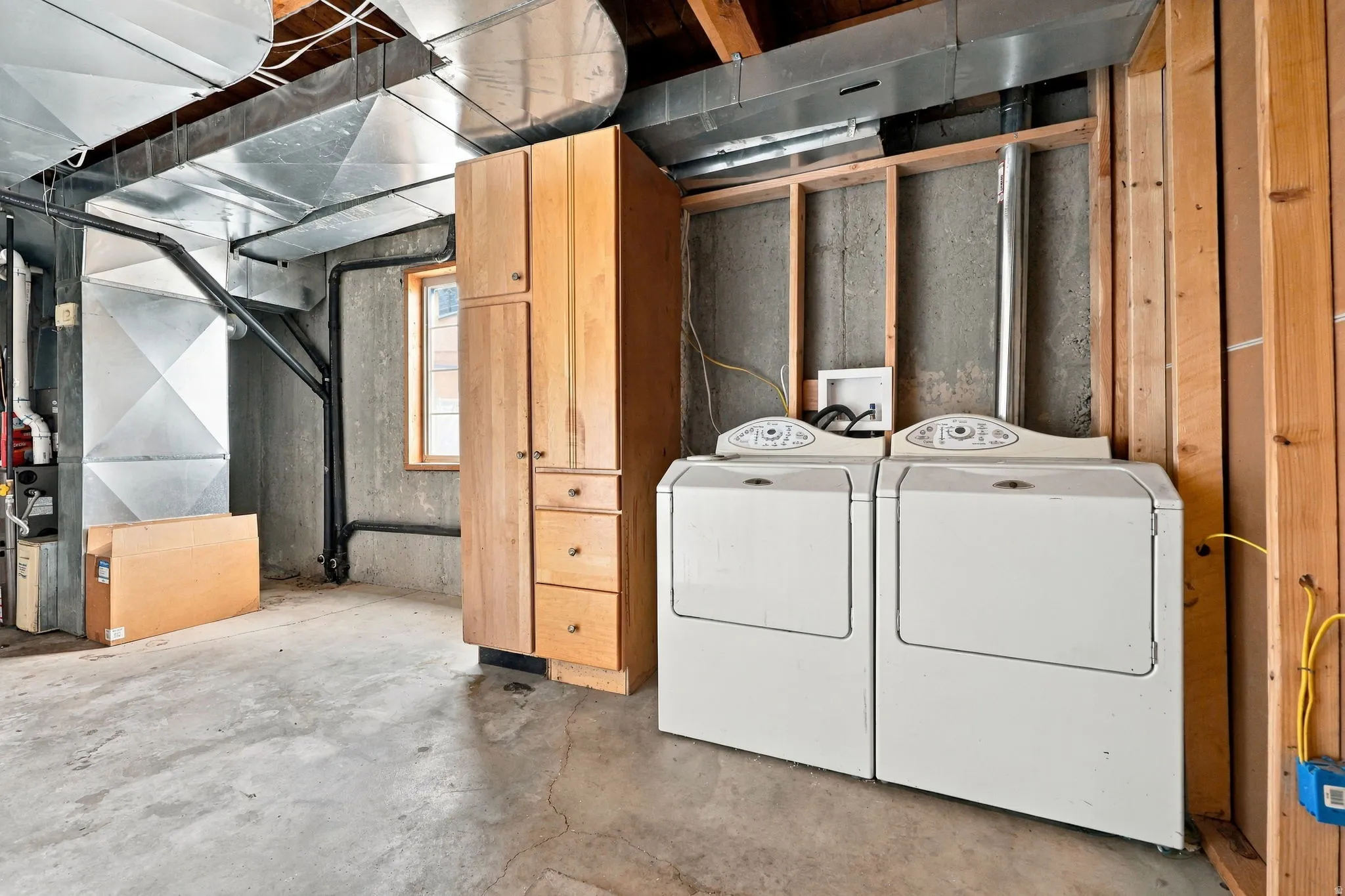 Laundry area with two appliances, wood-finish cabinetry, and exposed wood framing
