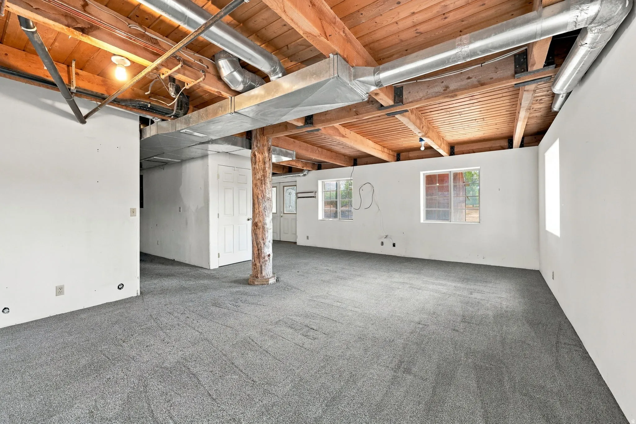 Exposed wood beam ceiling with ductwork and lighting, light gray carpet flooring, white walls, and multiple windows